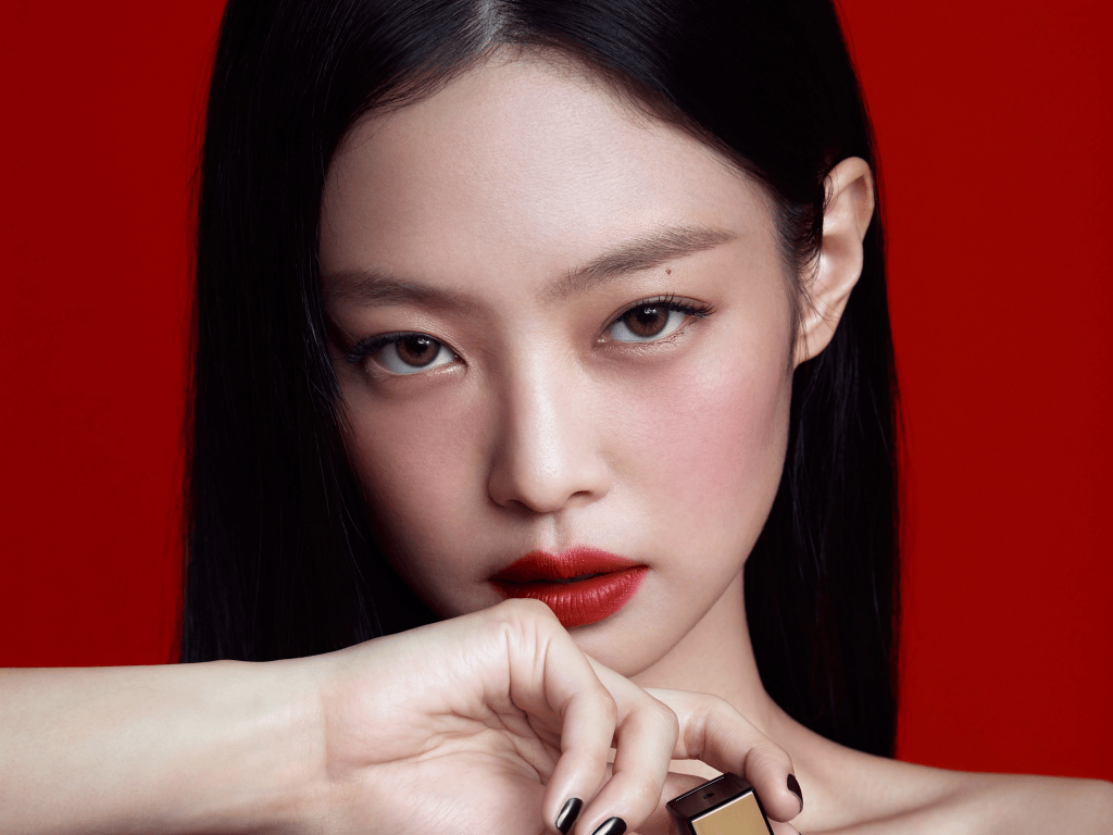 Close-up portrait of a woman with long black hair and bold red lipstick, set against a vibrant red background.